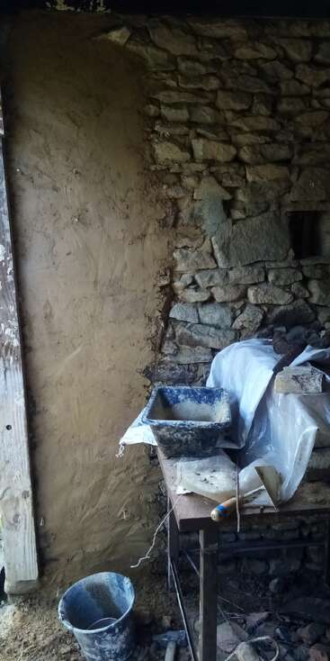 Nesta imagem, uma parede de pedra está sendo rebocada com lama fresca. Você pode ver ferramentas de construção, um balde e uma mesa coberta em primeiro plano.