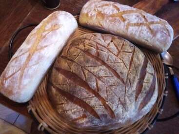 Esta imagem mostra três pães rústicos em uma cesta de vime, com belos padrões de pontuação em suas crostas, descansando em uma mesa de madeira.