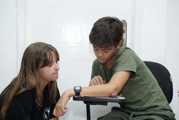 Un chico y una chica están sentados en casa. El chico apoya el brazo en un escritorio mientras la chica le mira con expresión seria.