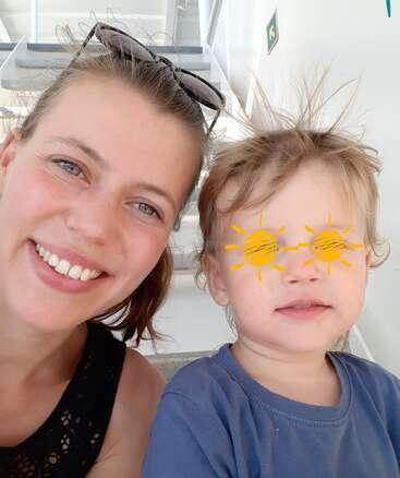 The image shows a woman and a child posing for a selfie, with the child\'s face blurred out and yellow suns drawn over their eyes.