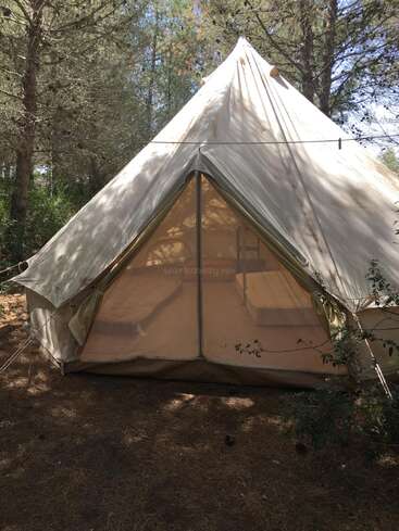 The image depicts a white canvas tent situated in a wooded area, with a central entrance and a prominent watermark reading \"workaway.info\" in the center.