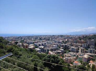 The image depicts a cityscape with a road, trees, and buildings, set against a blue sky with mountains visible in the distance.