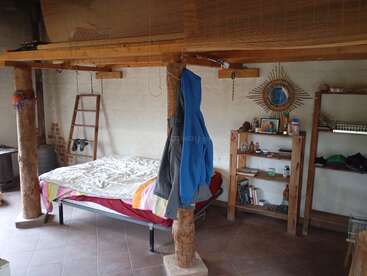 Cette chambre rustique et confortable se caractérise par un lit simple, des poutres en bois, des étagères, une échelle, des vestes suspendues, un sol carrelé et une décoration éclectique, créant ainsi une atmosphère chaleureuse et habitée.