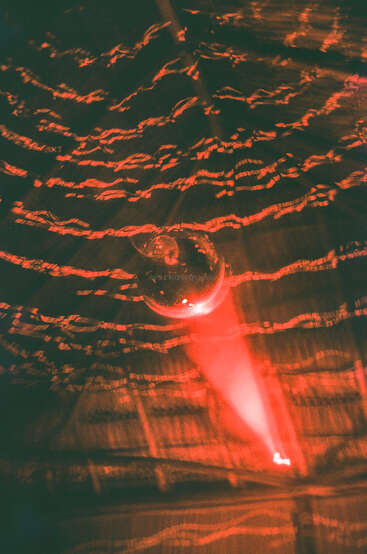 Eine glänzende Discokugel wirft wirbelnde rote Lichter an die dunkle Decke und schafft so eine energiegeladene, pulsierende Partyatmosphäre voller Bewegung und dynamischer Lichtmuster.