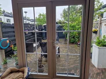 La imagen representa una serena escena de patio, con una puerta de cristal, plantas en macetas y un patio de ladrillo, con una sutil marca de agua en la que se lee "kawo" en el centro.