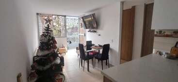 The image depicts a modern, minimalist living space with a Christmas tree, a dining table, and a kitchen island, featuring white walls and a large window.