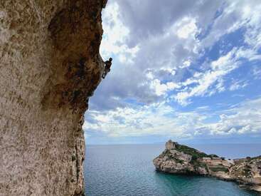 Ein Kletterer erklimmt eine steile Klippe über einem atemberaubend blauen Meer, während dramatische Wolken und eine felsige Insel in der Ferne eine abenteuerliche Szenerie bilden.