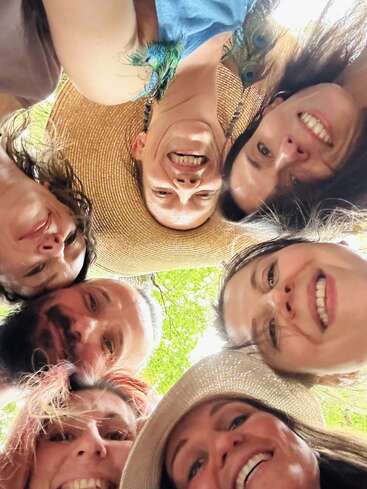 Un grupo de siete personas, sonrientes y felices, forman un círculo y miran a la cámara. Están al aire libre, rodeados de vegetación, disfrutando de la compañía de los demás.