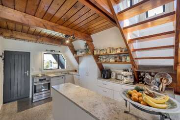 Esta acogedora cocina cuenta con vigas de madera, escaleras abiertas, una encimera de piedra, electrodomésticos modernos, estantes con tarros y un frutero, combinando estilos rústicos y contemporáneos.