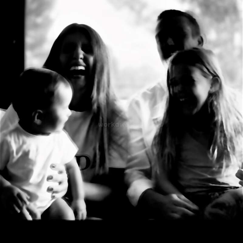 Das Bild ist eine Schwarz-Weiß-Fotografie einer vierköpfigen Familie, mit zwei Erwachsenen und zwei Kindern, die zusammensitzen und in die Kamera lächeln.