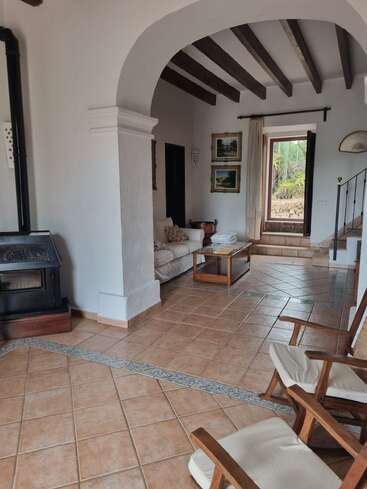 Este acogedor salón cuenta con suelos de baldosas, vigas de madera, paredes blancas, una chimenea, arcos, cómodos asientos, obras de arte, luz natural y vistas al exterior. Un ambiente acogedor.