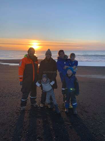 The image depicts a family of five standing on a beach at sunset, with the sun setting over the ocean in the background.