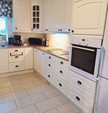 This kitchen features white cabinets, a built-in oven, electric stove, microwave, coffee maker, toaster, tiled floor, and a window with a patterned curtain.