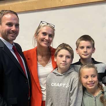 Das Bild zeigt eine fünfköpfige Familie, die für ein Foto posiert, mit dem Vater auf der linken Seite, der Mutter in der Mitte und den drei Kindern zu ihrer Rechten.