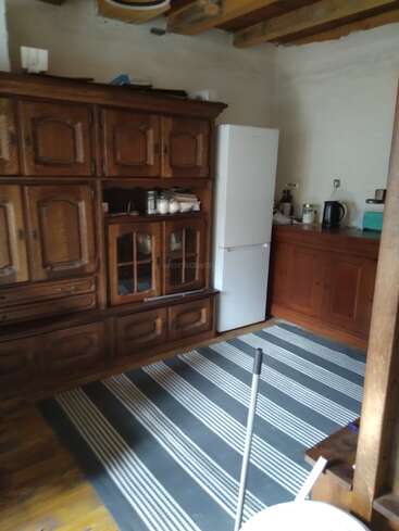 Cette image montre une cuisine rustique avec des armoires en bois, un réfrigérateur blanc, un tapis rayé, des poutres apparentes au plafond, une bouilloire et divers ustensiles de cuisine sur le comptoir.