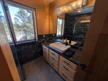 Dieses Badezimmer besticht durch ein modernes Design mit einem Aufsatzwaschbecken, einem großen Spiegel, einer Granitarbeitsplatte, dunkel gemusterten Wänden, geräumigen Schubladen, viel Tageslicht und einem Blick ins Grüne.