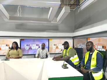Quatre personnes sont assises dans un studio de télévision pour un talk-show intitulé "Good Morning Gambia". Deux hommes portent des gilets réfléchissants et des microphones sont posés sur la table.