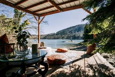 The image depicts a serene outdoor setting, featuring a wooden structure, a body of water, and a tree, evoking a sense of tranquility and natural beauty. The scene is likely a park or recreational area.