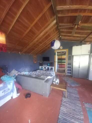 Cette chambre chaleureuse est dotée d'un plafond en bois en pente, d'un mobilier sobre, d'un lit, d'un sol recouvert de tapis, d'un réfrigérateur, d'un éclairage tamisé et d'une lanterne en papier, créant ainsi une ambiance rustique et chaleureuse.