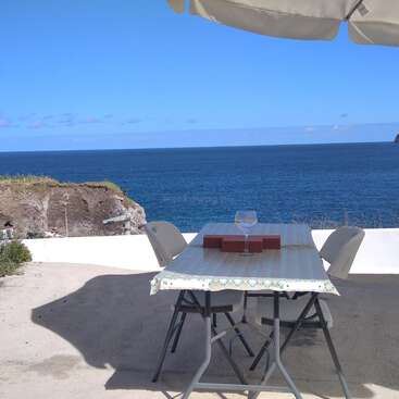 La imagen representa un entorno sereno al aire libre, con una mesa y sillas, y una gran masa de agua al fondo, que evoca una sensación de tranquilidad y relajación.