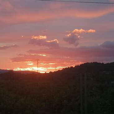 Un coucher de soleil éclatant teinte le ciel de nuances roses, orangées et violettes. Les collines et les nuages se découpent en silhouette, rehaussant ce paysage vespéral paisible, pittoresque et serein.