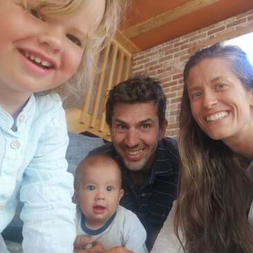La imagen muestra a una familia de cuatro miembros posando para un selfie, con un niño pequeño a la izquierda, un bebé en el centro y un hombre y una mujer a la derecha, todos sonriendo.