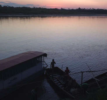 The image depicts two people standing on a boat in a body of water, with another boat nearby, set against a serene sunset backdrop.