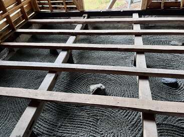 This image shows a wooden framework over a Zen rock garden with raked gravel patterns and embedded stones, viewed from above inside a partially constructed structure.