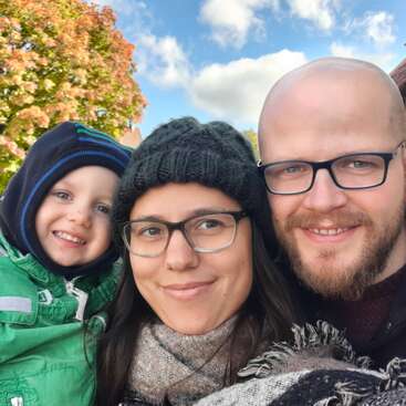 La imagen muestra a una familia de tres miembros posando para un selfie, con la mujer en el centro con gafas y gorro de punto, rodeada por un niño y un hombre a cada lado.