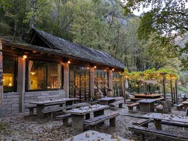 Ce restaurant rustique en plein air est situé dans une zone boisée. Il est doté de tables et de bancs en pierre, de guirlandes lumineuses chaleureuses et d'un environnement verdoyant qui évoquent une atmosphère paisible et chaleureuse.