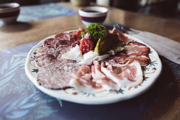 Assiette de charcuteries assorties, salami, prosciutto et viandes froides, garnie de cornichons, de persil et de tomates, servie sur un plat décoré. Table rustique.