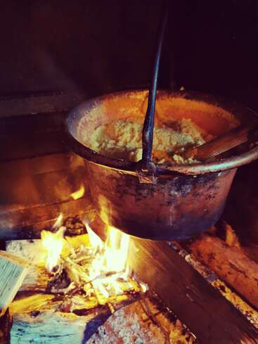 Une marmite rustique en cuivre est suspendue au-dessus d'un feu de bois ouvert, en train de cuire des aliments traditionnels. Les flammes chauffent doucement la marmite, créant une atmosphère chaleureuse de cuisine à l'ancienne.