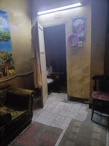 Ein schummriger Raum mit abgenutzten Möbeln, einer offenen Tür, Wandkunst, einem Spiegel und sichtbaren Fliesen. Gemütlich und doch alt, mit persönlicher Note und bescheidenem Dekor.