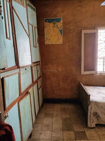 Cette petite chambre rustique est dotée d'armoires en bois bleu clair, d'un lit simple recouvert d'un couvre-lit à motifs floraux, d'un sol carrelé, d'une fenêtre ouverte, de murs marron et d'une carte.