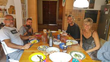 La imagen muestra a un grupo de personas reunidas en torno a una mesa, probablemente disfrutando de una comida. La escena tiene como telón de fondo un comedor o una cocina.