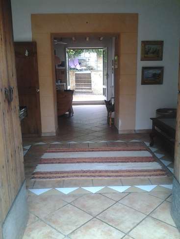 La imagen representa el interior de una casa, con suelo de baldosas, puerta de madera y un portal que conduce a una zona exterior con un patio y un pequeño perro cerca.