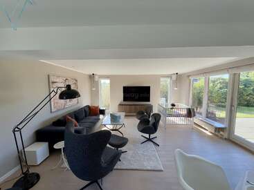 Le salon moderne est composé de fauteuils élégants, d'un canapé épuré, d'un lampadaire, d'une télévision, d'un parc pour enfants, de grandes fenêtres avec vue sur le jardin et d'une lumière naturelle, créant ainsi une atmosphère chaleureuse.