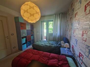 Cette chambre confortable comprend deux lits, des étagères cubiques colorées, un papier peint à motifs représentant des maisons, une suspension originale, un bureau, une fenêtre avec des rideaux et une vue sur l'extérieur.