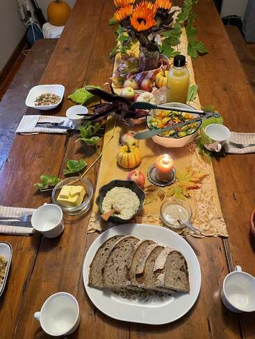 Ein rustikaler Herbsttisch mit Sonnenblumen, Brot, Butter, Reis, Salat, Kürbissen, einer Kerze, Saft und festlicher Dekoration, der eine gemütliche Ernteatmosphäre schafft.