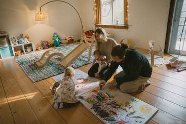 Una familia pasa un buen rato junta en una acogedora sala de juegos, dibujando en un gran papel, con juguetes, un tobogán y la cálida luz del sol llenando el espacio.