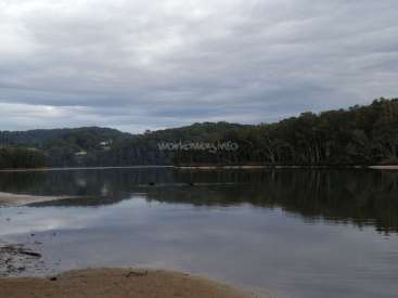 A imagem retrata uma cena serena de um lago com uma praia de areia em primeiro plano, cercada por árvores e um céu nublado, evocando uma sensação de tranquilidade.