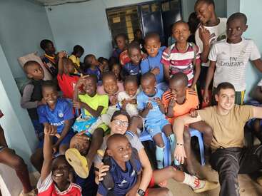 Un alegre grupo de niños y dos adultos posan juntos en un interior, vestidos con coloridos atuendos deportivos. El ambiente es animado, alegre y lleno de caras juguetonas y sonrientes.