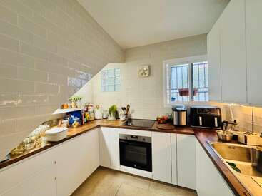 Diese Küche besticht durch weiße Schränke, Arbeitsplatten aus Holz, moderne Geräte, Pflanzen, Gläser und Küchenutensilien. Ein Fenster und Glasbausteine sorgen für Tageslicht und schaffen so einen einladenden, aufgeräumten Raum.