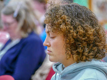 The image depicts a young person with curly hair, wearing a light blue hoodie, set against a blurred background of people in the distance.