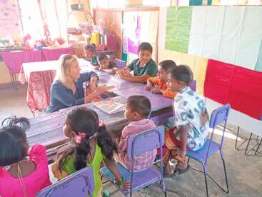 Un groupe de jeunes enfants est assis autour d'une table avec un enseignant dans une salle de classe colorée, participant ensemble à une activité d'apprentissage vivante et interactive.