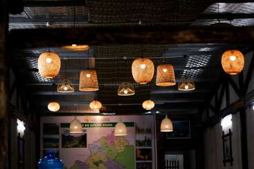 Warm, woven lamps hang from the ceiling in a cozy, dimly-lit room. Maps and photos decorate the far wall, creating a welcoming, rustic ambiance.