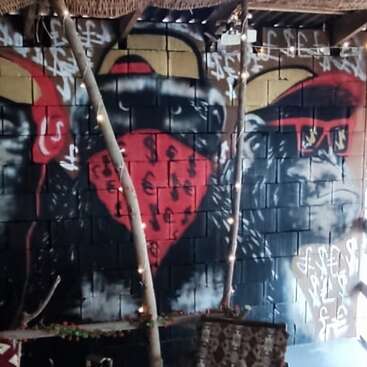 Dieses Bild zeigt Graffiti-Kunst an einer Wand mit drei stilisierten Affen. Sie tragen Hüte, Sonnenbrillen und Bandanas mit Währungssymbolen und sind von Graffiti-Tags umgeben.
