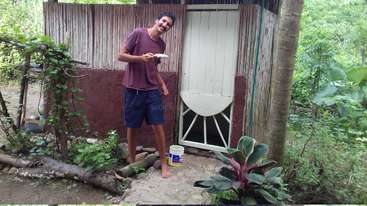 The image shows a person standing in front of a building, with a large window and a door. The building appears to be a house or a business, but the context is unclear.