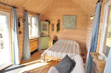 Dieses gemütliche Schlafzimmer im Holzhüttenstil verfügt über ein Doppelbett, zartblaue Vorhänge, rustikale Möbel, große Fenster, die für viel Tageslicht sorgen, eine schlichte Einrichtung und eine einladende, warme Atmosphäre.
