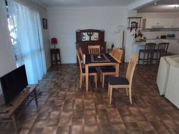 Esta imagen muestra un acogedor comedor con una mesa de madera y seis sillas, televisión, armario, taburetes de bar, cocina, lámpara y baldosas marrones estampadas.
